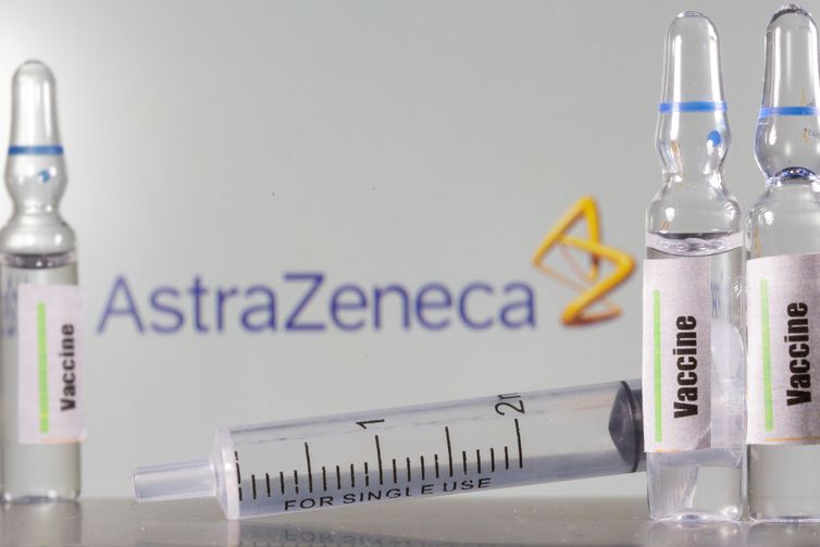 um tubo de ensaio etiquetado com a vacina &amp;eacute; visto na frente do logotipo da AstraZeneca