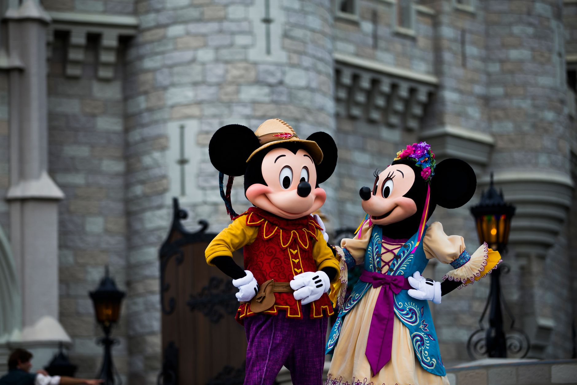 Mickey e Minnie Mouse em trajes coloridos fora de um cenário de castelo icônico.
