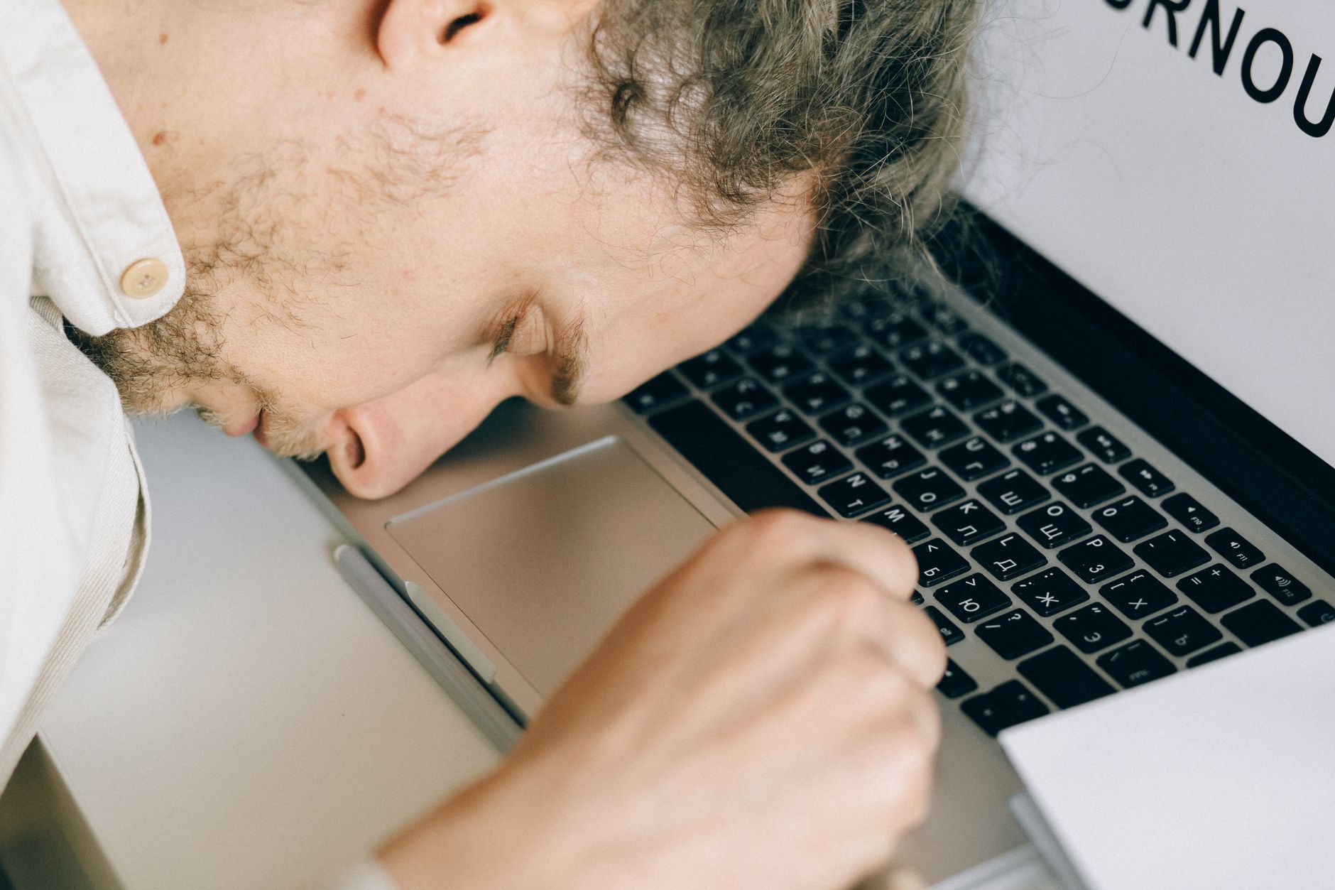 Funcionário exausto descansando a cabeça no teclado do laptop devido ao burnout e estresse.