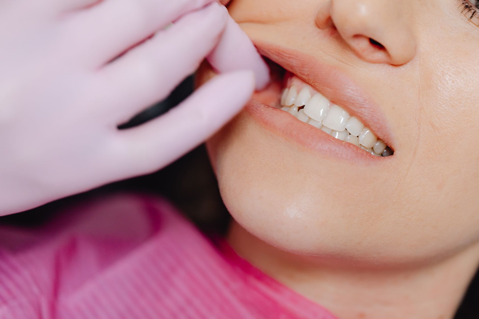 A mão enluvada de um dentista inspecionando os dentes de uma paciente durante um exame.