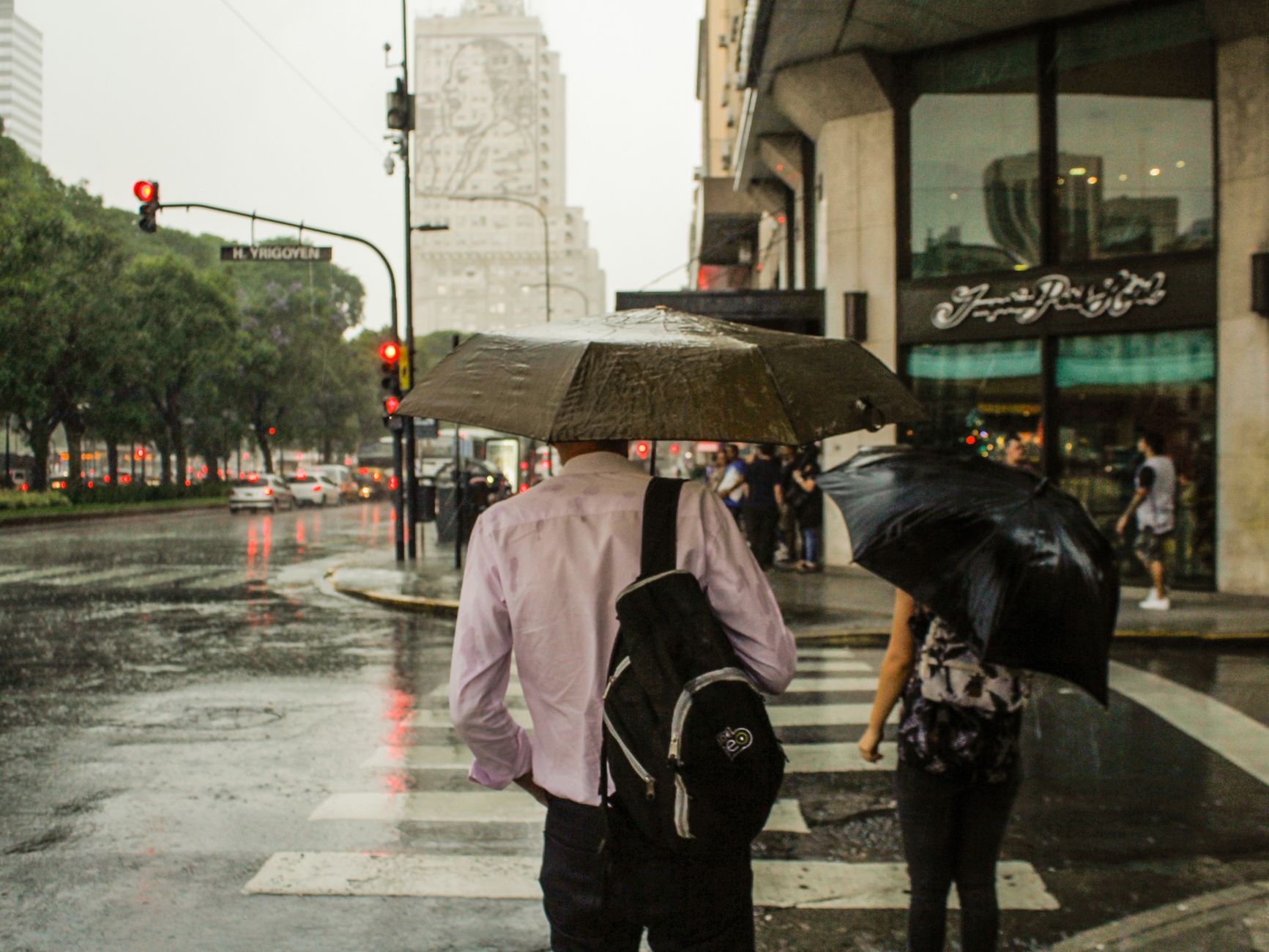 Pedestres com guarda-chuvas atravessando a rua em um dia chuvoso em Buenos Aires, Argentina.