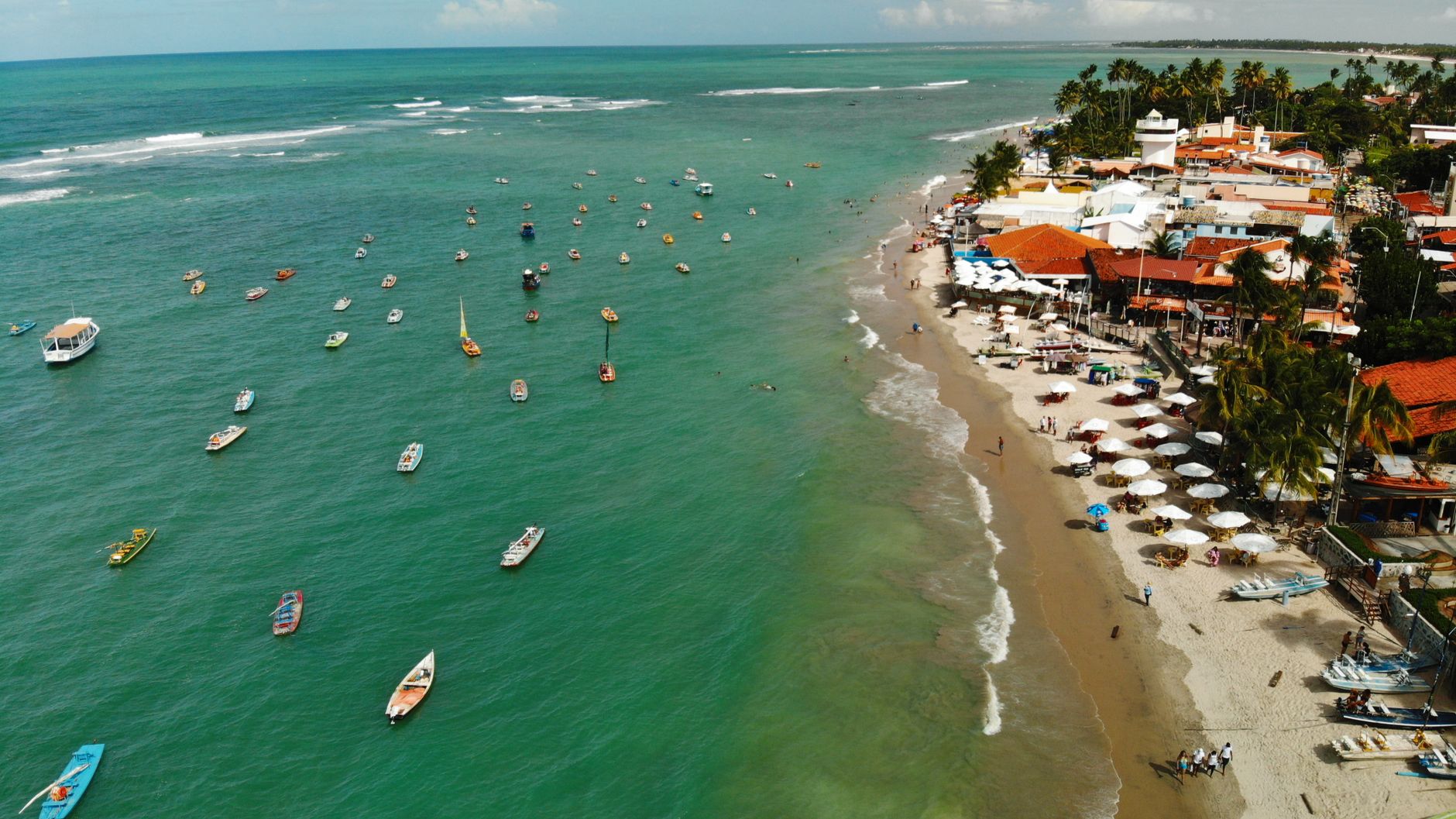 Uma deslumbrante vista aérea da praia de Porto de Galinhas com barcos e vibrantes resorts à beira-mar.