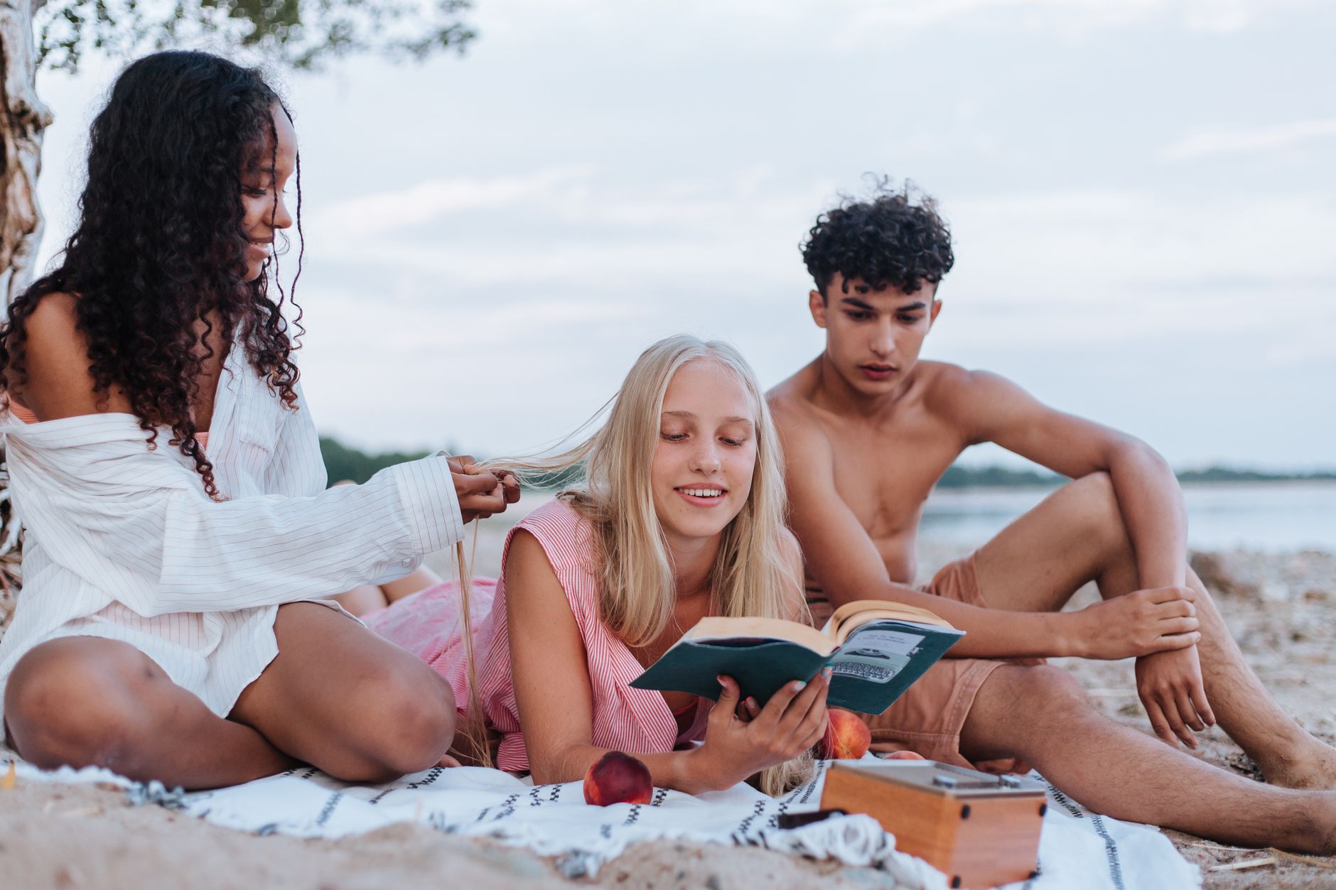Três adolescentes relaxando na praia, lendo e desfrutando de um piquenique de verão juntos.
